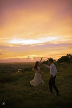 a man and woman are dancing in the grass at sunset with their arms outstretched to each other