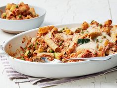 two white bowls filled with pasta and meat on top of a table next to a striped napkin