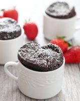 two mug cakes with chocolate frosting and strawberries in the background on a table