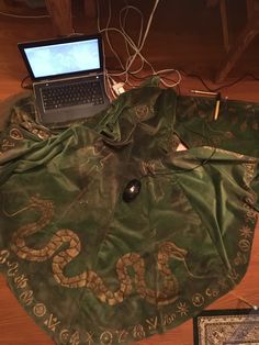 an open laptop computer sitting on top of a green cloth covered table next to a book