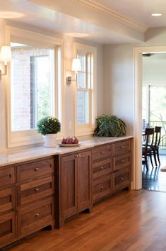 a kitchen with wooden cabinets and white counter tops next to a dining room table in front of two large windows