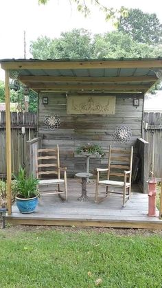 an outdoor patio with chairs and table in the grass next to a wooden structure that has writing on it