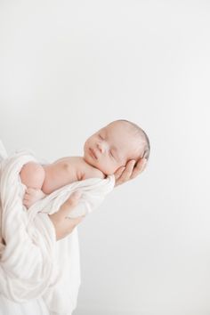 a woman holding a baby wrapped in a white blanket while she holds it up to her face