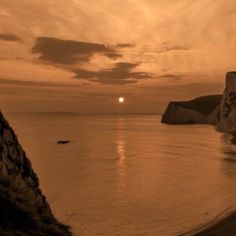 the sun is setting over the ocean with cliffs on either side and water in the foreground