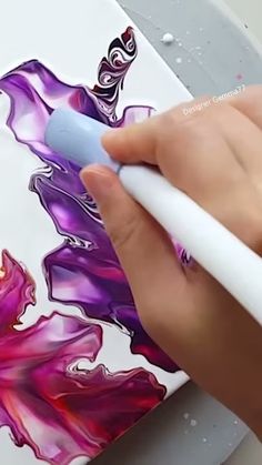 a person is drawing on an ipad with a white pen and some watercolors