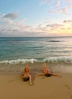 two women laying on the beach with their feet in the sand