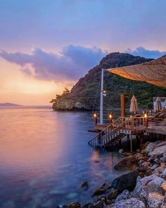 an outdoor dining area with umbrellas and chairs on the water at sunset or dawn