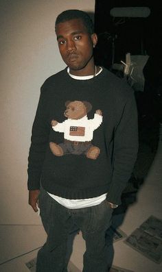 a man standing in front of a wall wearing a sweater with a teddy bear on it