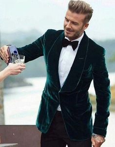 a man in a green velvet jacket and bow tie is holding a drink while another man looks on