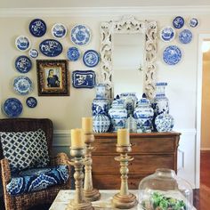 blue and white plates are on the wall above a table with candles, vases and a mirror