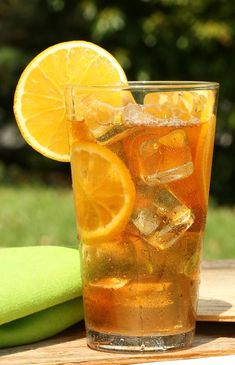 a glass filled with ice and lemon slices on top of a wooden table next to a green towel