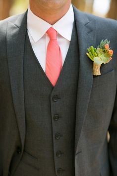 a man wearing a gray suit with a red tie and flower boutonniere