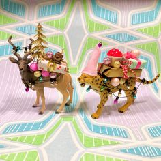 two small figurines are sitting on top of a colorful surface with trees and presents