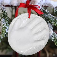 a white ornament hanging from a christmas tree with snow on it and a red ribbon