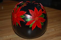 a black vase with red poinsettias painted on it's sides sitting on a wooden table