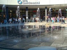 many people are walking around in front of a water fountain