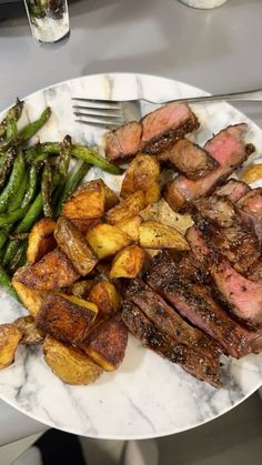 steak, potatoes and green beans on a white plate with silverware next to it