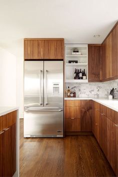 a kitchen with wooden cabinets, stainless steel refrigerator and wood flooring that has white marble countertops