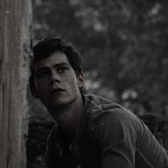 a young man sitting next to a tree in the woods looking off into the distance