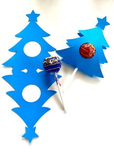 two lollipops sitting on top of blue paper cut outs with christmas trees in the background