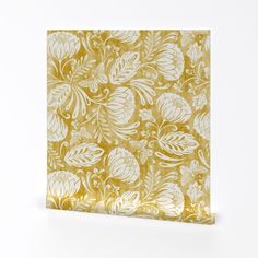 a gold and white paper with leaves on it, sitting against a white wall background