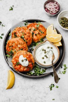 salmon patties with capers and white sauce on a plate next to lemon wedges