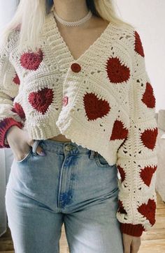 a woman wearing a red and white crochet sweater with hearts on the sleeves