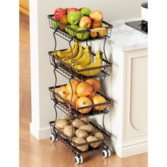 three tiered fruit rack with bananas, apples, and potatoes on wheels in front of a kitchen counter