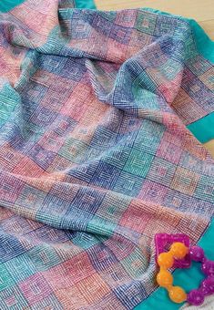 a colorful blanket laying on top of a wooden floor next to a pair of scissors