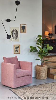 a living room with pink furniture and pictures on the wall above it, along with a plant in a wicker basket