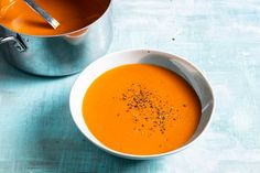 there is a bowl of carrot soup and a pot of soup on the table next to it