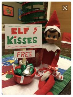 an elf is holding a sign that says elf kisses free and there are candy on the table