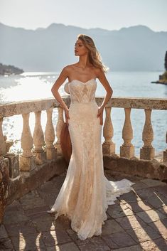 a woman in a wedding dress standing on a balcony near the water with her hands on her hips