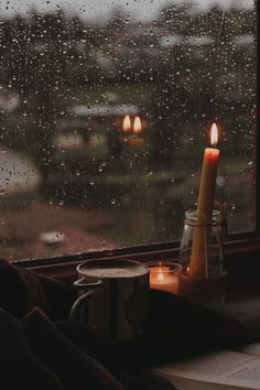 a candle is sitting on a window sill next to a book and coffee cup