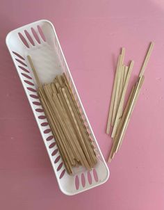 several wooden sticks in a white container on a pink surface