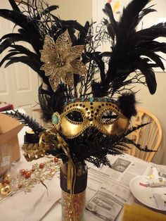 a masquerade mask sitting on top of a table next to a vase filled with feathers