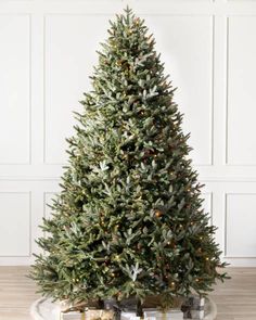 a small christmas tree with lights and presents on the floor in front of a white wall