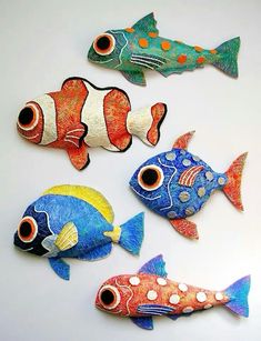 four colorful fish are sitting on a white surface, one is painted orange and the other is blue