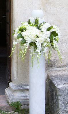 a tall white vase filled with flowers on top of a stone floor next to a doorway