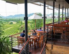 people are sitting at wooden tables on the deck overlooking green hills and valleys in the distance