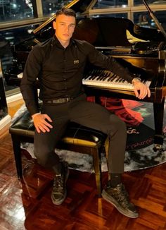 a man sitting at a piano in front of a window with the city lights behind him