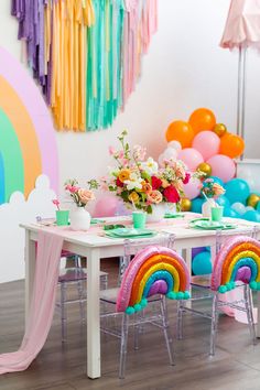 the table is set with balloons, flowers and other decorations for a rainbow themed birthday party