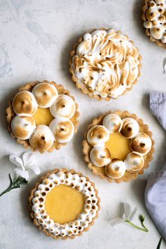 four small pies with white frosting and flowers around them on top of a table