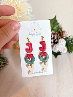 a pair of red and green earrings sitting on top of a wooden table next to a christmas tree