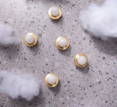 three white and gold knobs sitting on top of a gray surface next to clouds