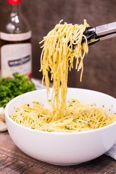 someone is lifting spaghetti out of a white bowl with parmesan cheese on the side