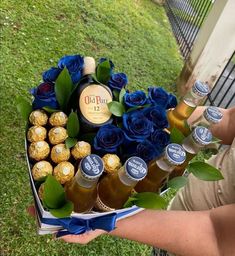 a person holding a box filled with blue roses and bottles of beer next to some chocolates