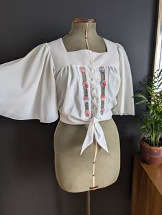 Gorgeous 70's Woodstock/California vibes vintage top with Angel wings. Button and tie round waist.  Good condition apart from a bit of fabric snagging. Shown in photos. 100% Triacetate Would look gorgeous with a pair of highwaisted jeans. Size UK 10/12/14 Depending on fit - Mannequin is a size 8 Chest 34-38 inches  The bust is actually open so hard to measure but going on the waist I'd say it would fit between a size 34 and 38 inch bust.  Waist 35 inches (untied, can be made smaller) Length 18 i Vintage Fitted Blouse For Festival, Retro Short Sleeve Top With Floral Embroidery, Retro Summer Tops With Floral Embroidery, Retro Floral Embroidered Summer Tops, Retro Embroidered Summer Tops, Vintage Blouse For Spring Festival, Vintage Spring Festival Blouse, Retro Fitted Blouse With Floral Embroidery, Fitted Vintage Tops With Floral Embroidery