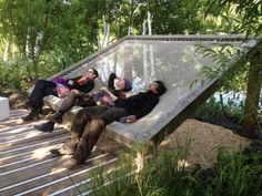 four people are lounging on a deck in the shade, with trees and water behind them