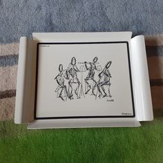 a white tray with some drawings in it on a green carpeted floor next to a blue towel